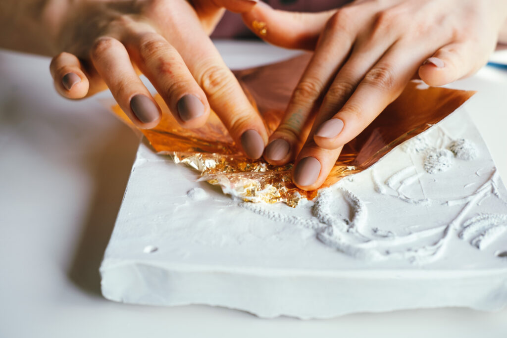 Close-up female hands working with plaster relief and golden foil. DIY and art hobby concept.