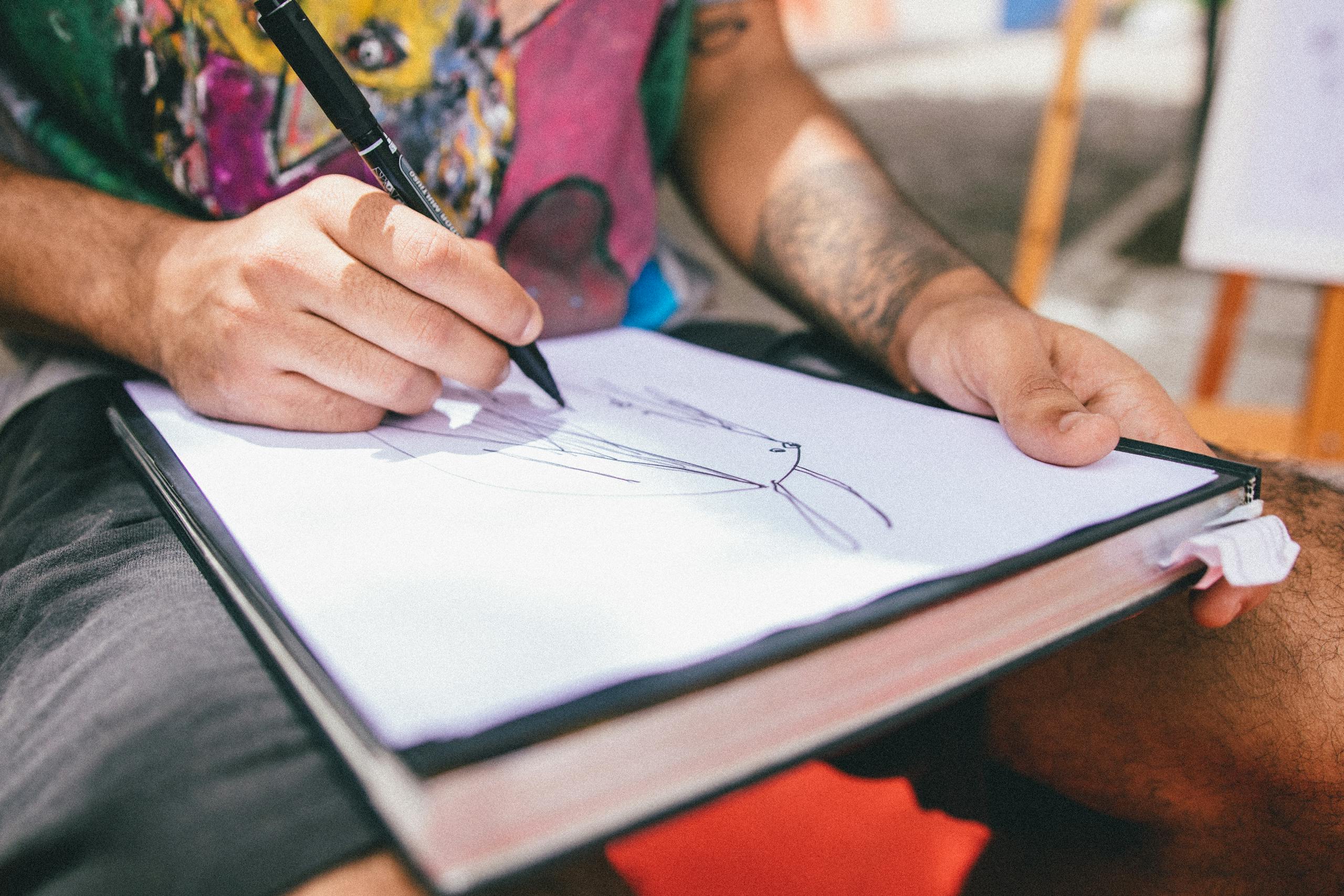 Close-up of a person drawing on a sketchpad with vibrant colors in an outdoor setting.
