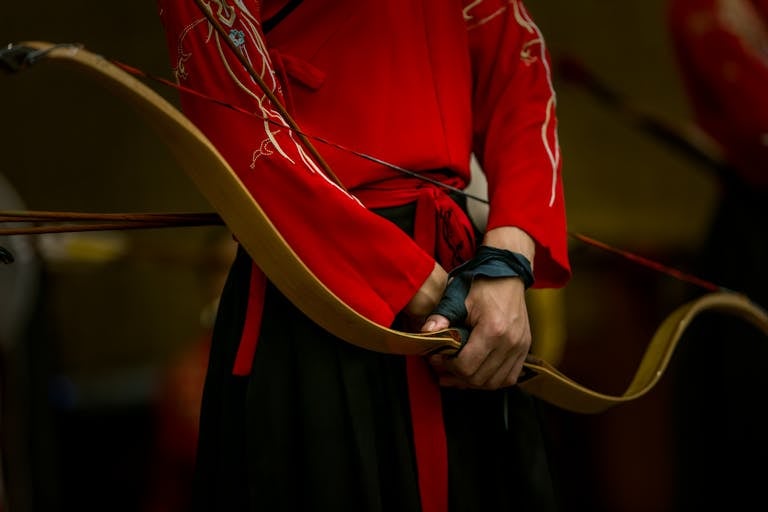 Close-up of an archer in traditional red clothing holding a longbow, showcasing cultural heritage.