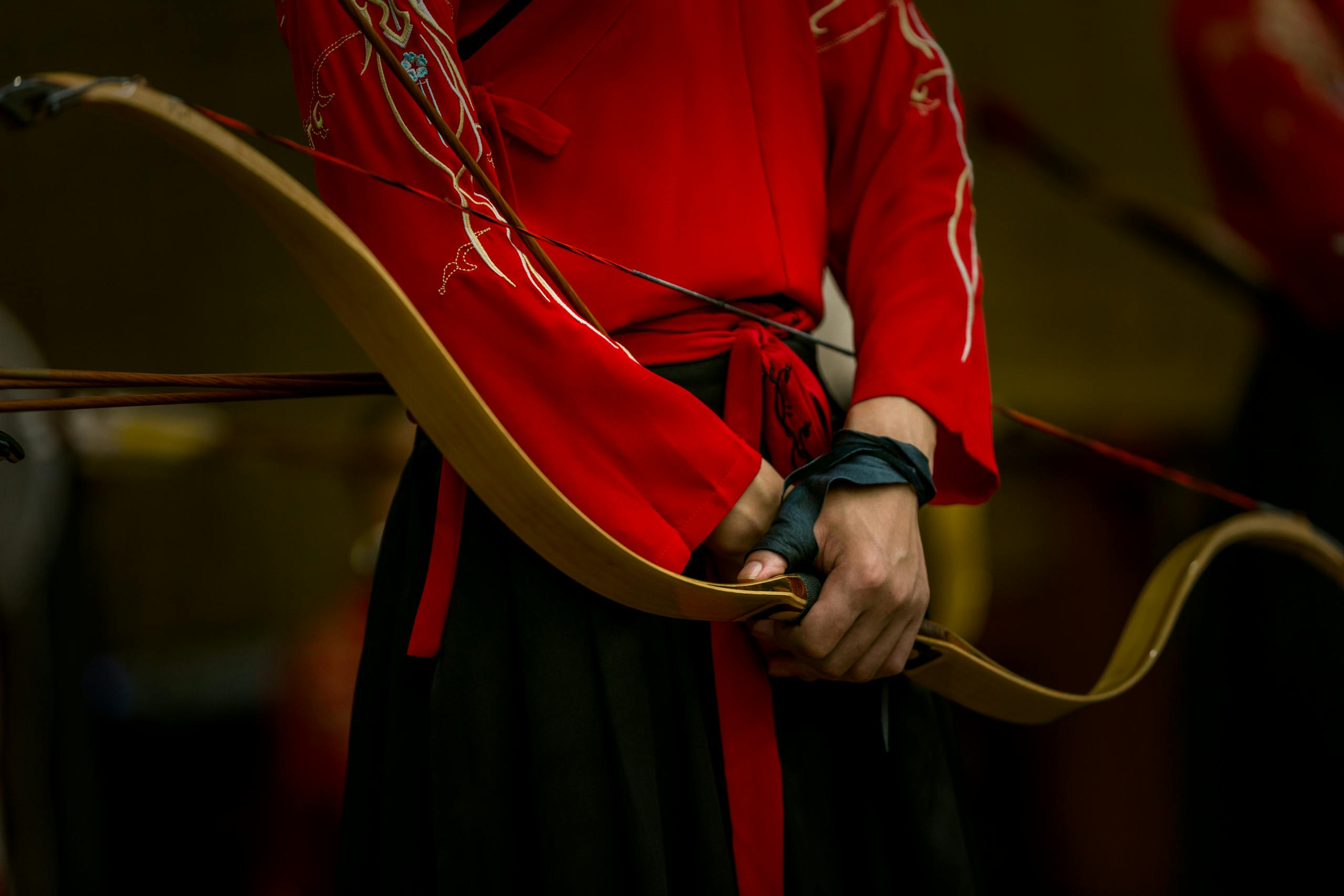 Close-up of an archer in traditional red clothing holding a longbow, showcasing cultural heritage.
