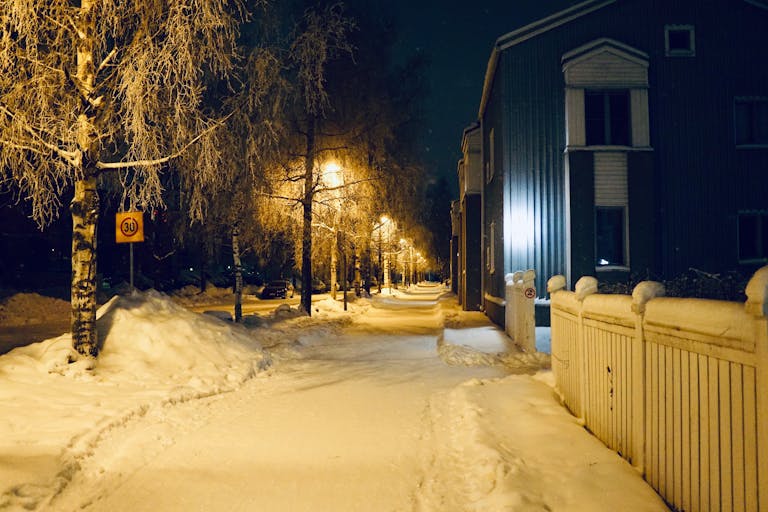A serene snowy street in Oulu, Finland, illuminated by warm streetlights on a winter night.