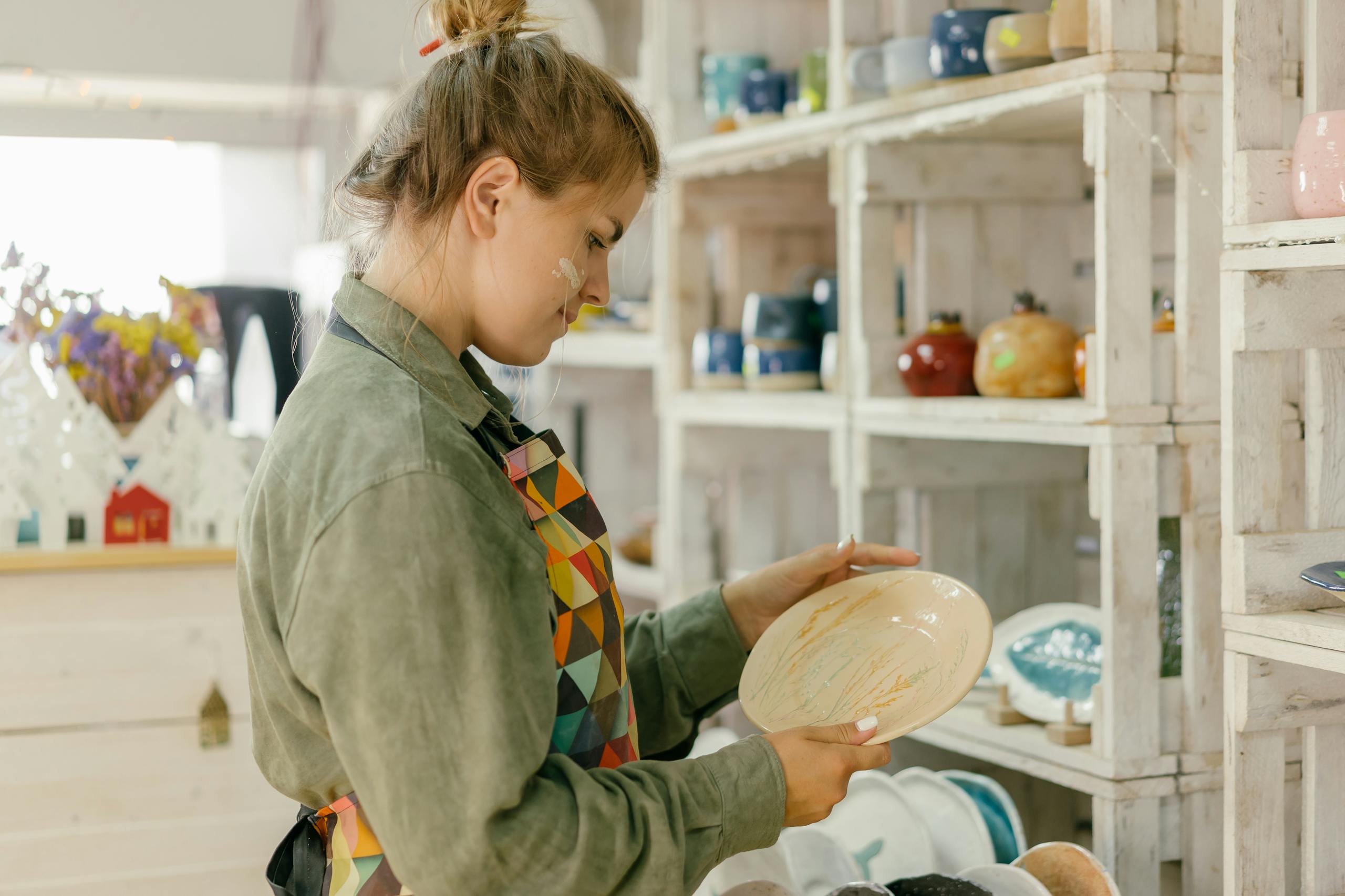 A woman in her studio examines a handmade ceramic plate, focusing on craftsmanship.