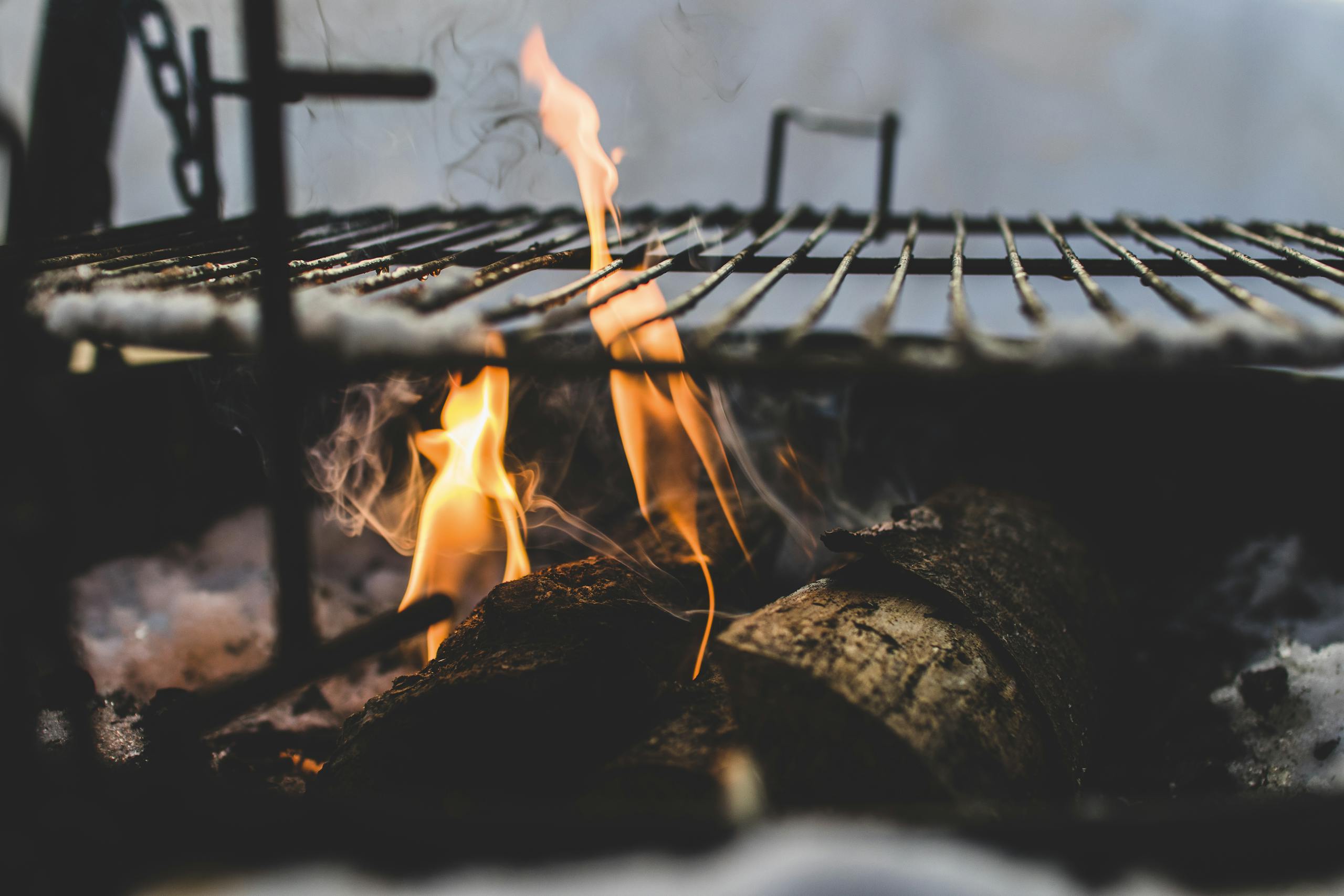 Close-up view of firewood burning in a fire pit with a metal grill above, outdoor setting.