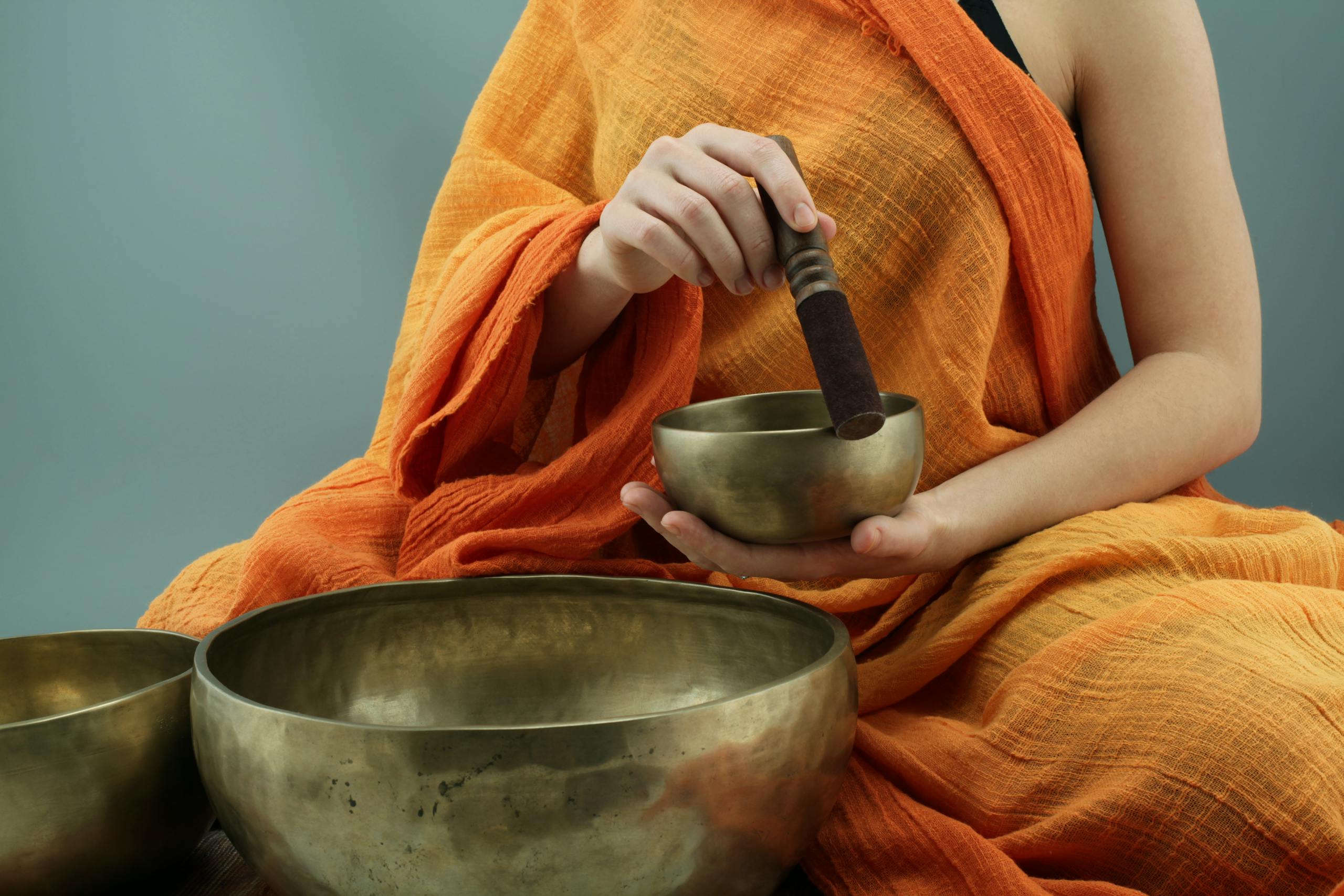 Person in traditional attire using Tibetan singing bowls in a meditative practice.