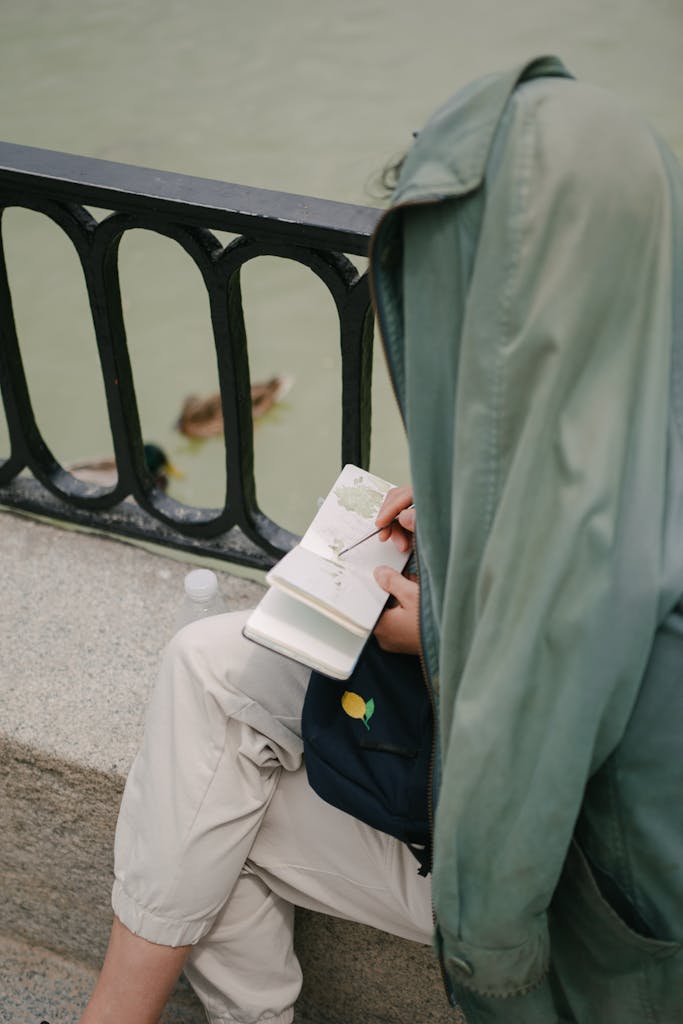 Person sketching near a river in Madrid, Spain, with ducks visible in the background.