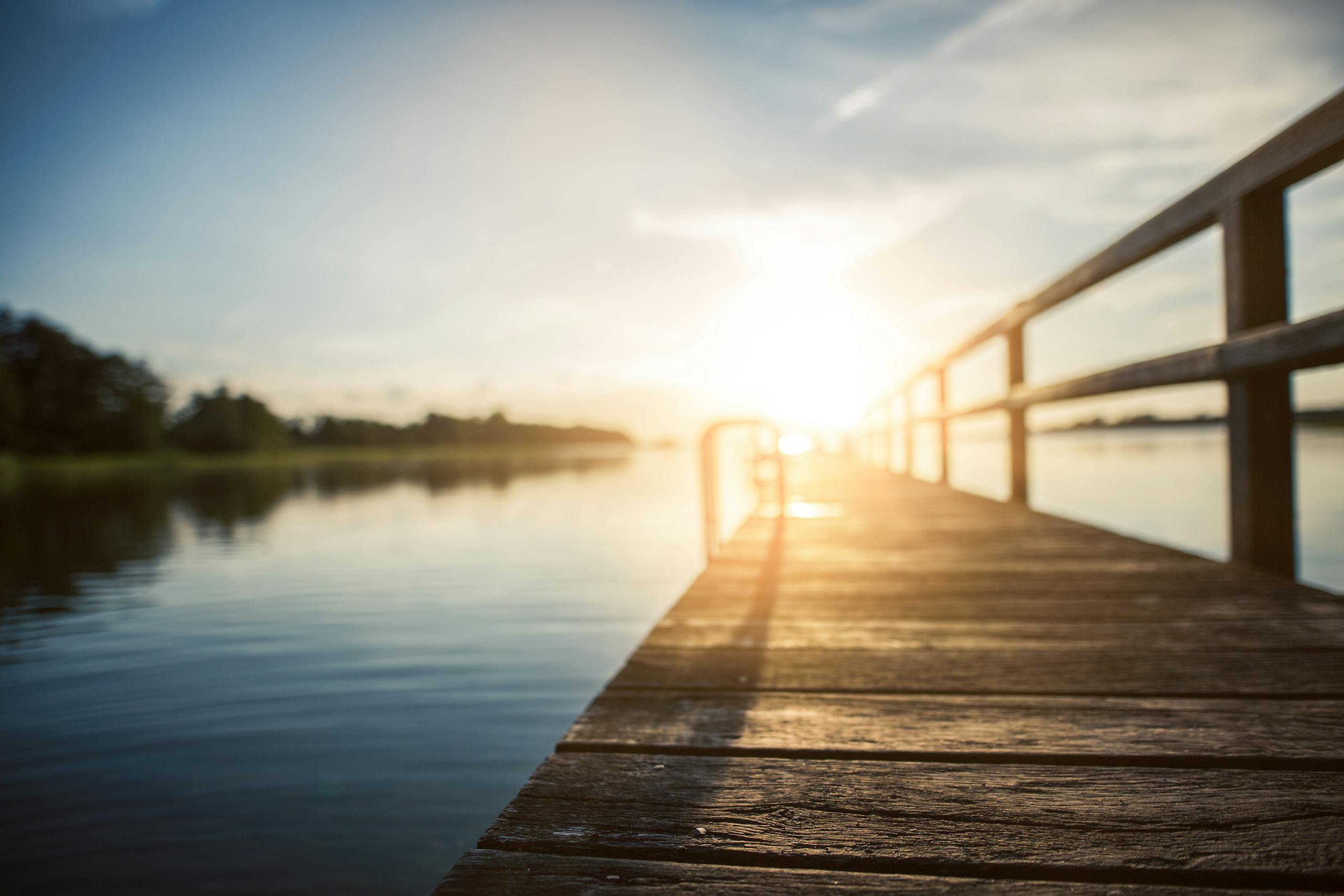 Peaceful sunset over a calm lake, captured from a wooden boardwalk in Kiel, Germany.