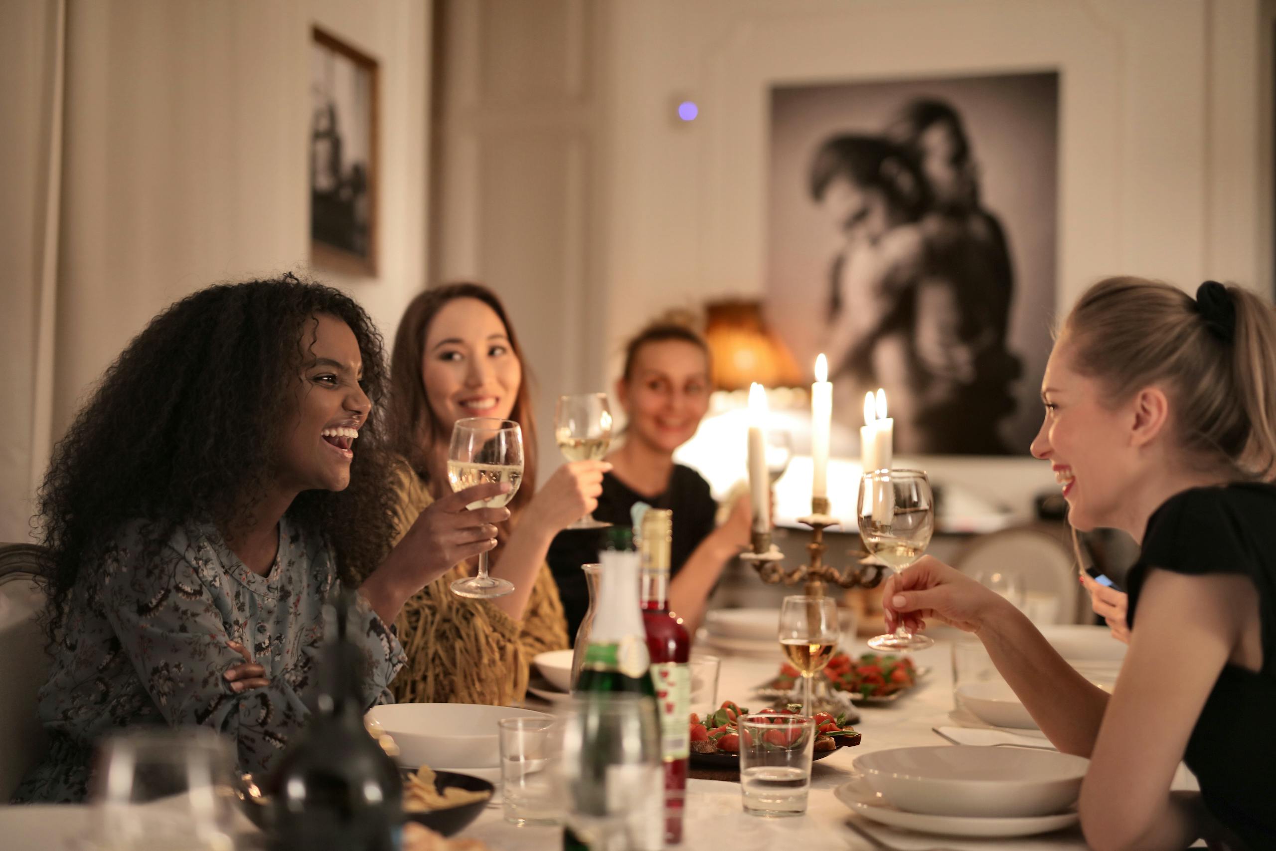 A group of diverse women enjoying candlelit dinner, sharing laughter and wine indoors.