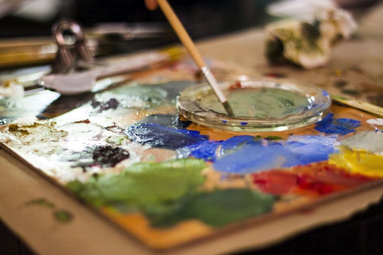 Creative close-up of an artist's palette with vibrant colors and a paintbrush indoors.