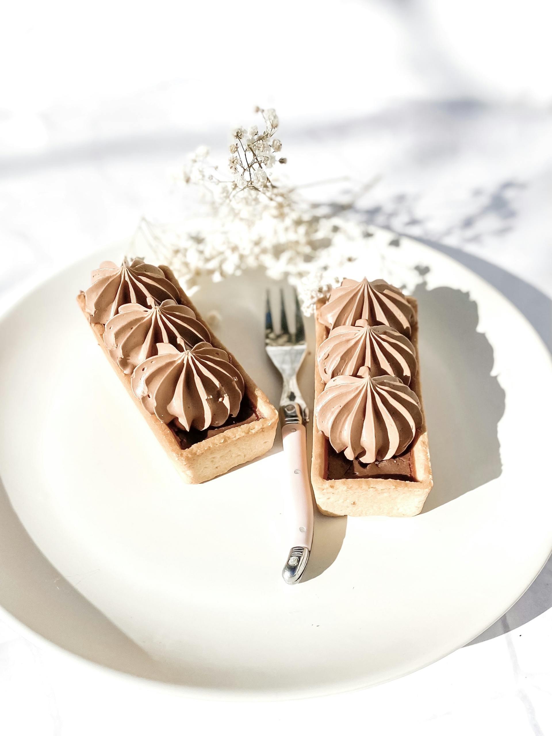 Elegant cream pastries on a plate with a fork, showcasing a sophisticated dessert arrangement.