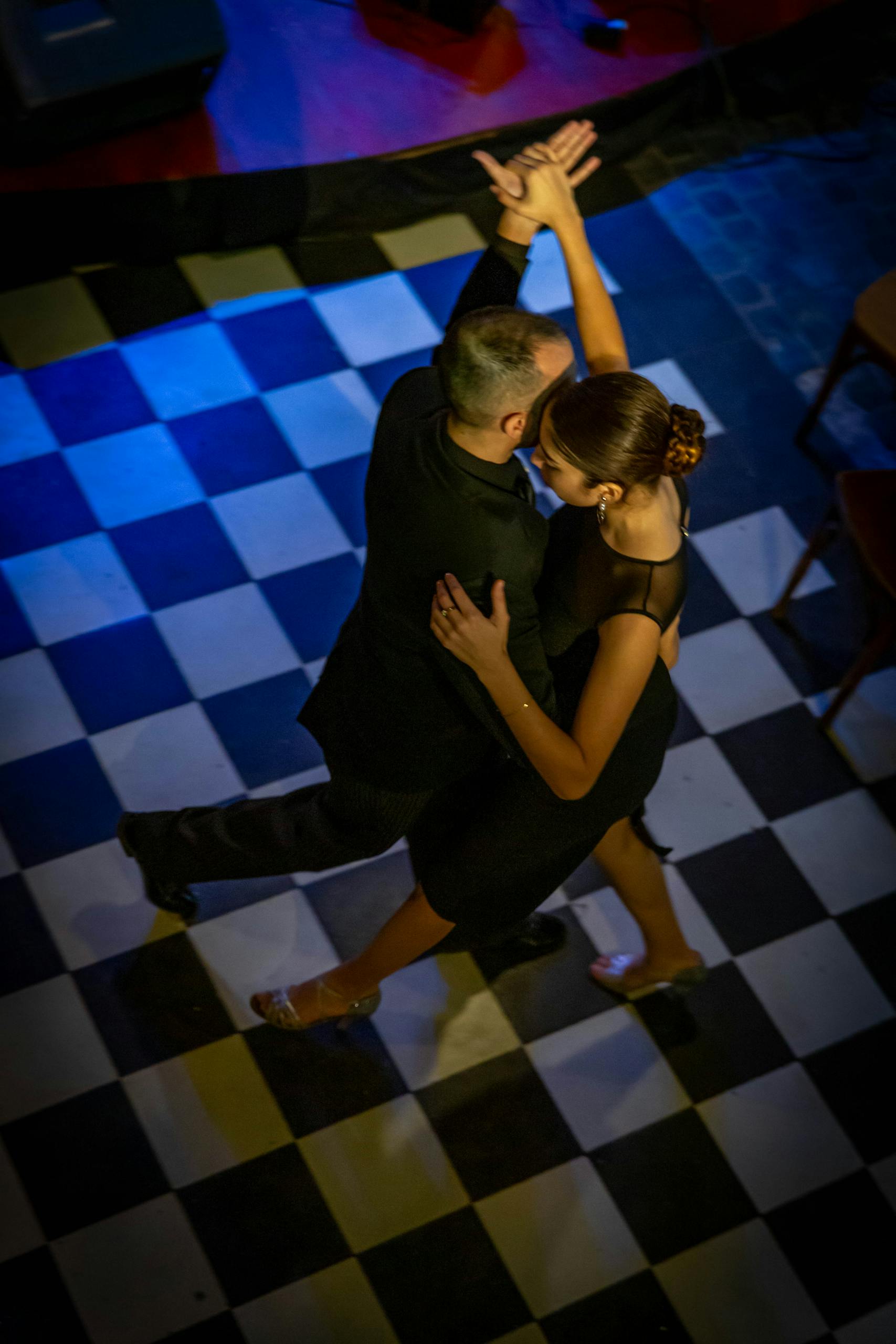 Top view of a couple performing tango on a checkered floor in a dimly lit setting.