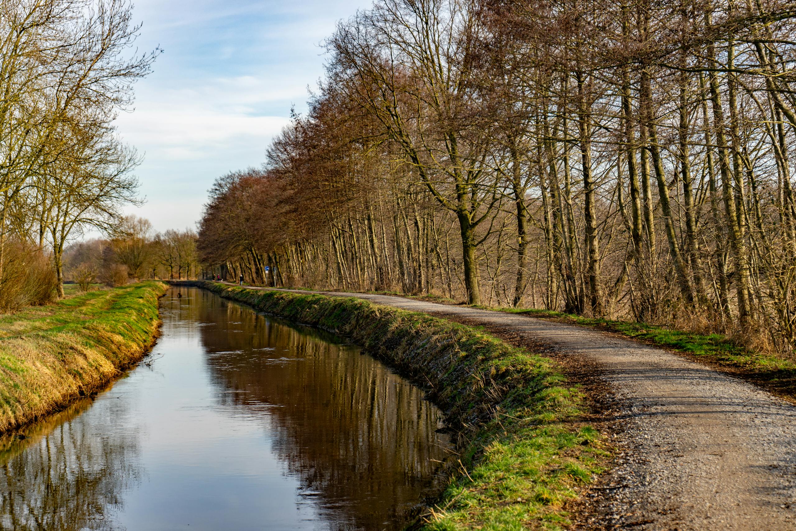 Peaceful riverside path flanked by trees in Rietberg, Germany, perfect for a tranquil walk.