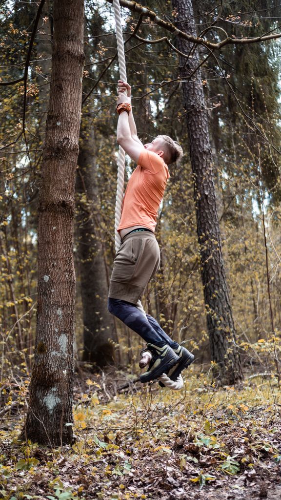 Adult male climbs a rope in a forest, showcasing strength and determination.